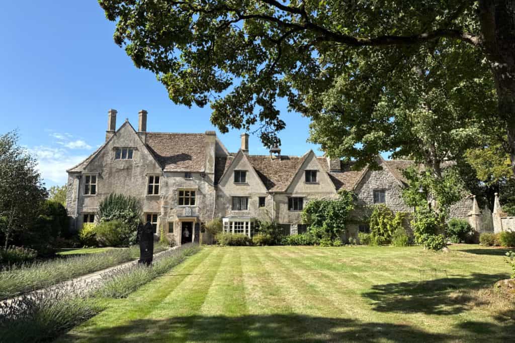 The frontage of Avebury Manor complete with a mowed lawn, ancient trees and blue sky