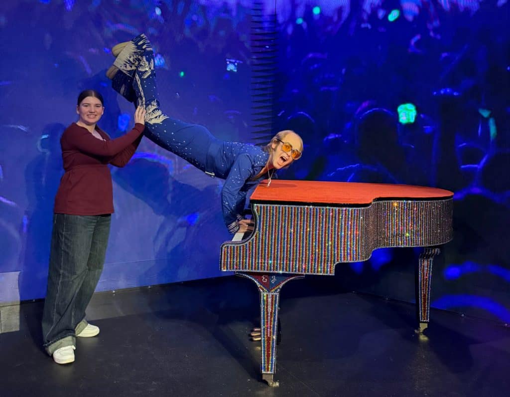 My daughter holding up the legs of the Elton John waxwork while he appears to play the piano