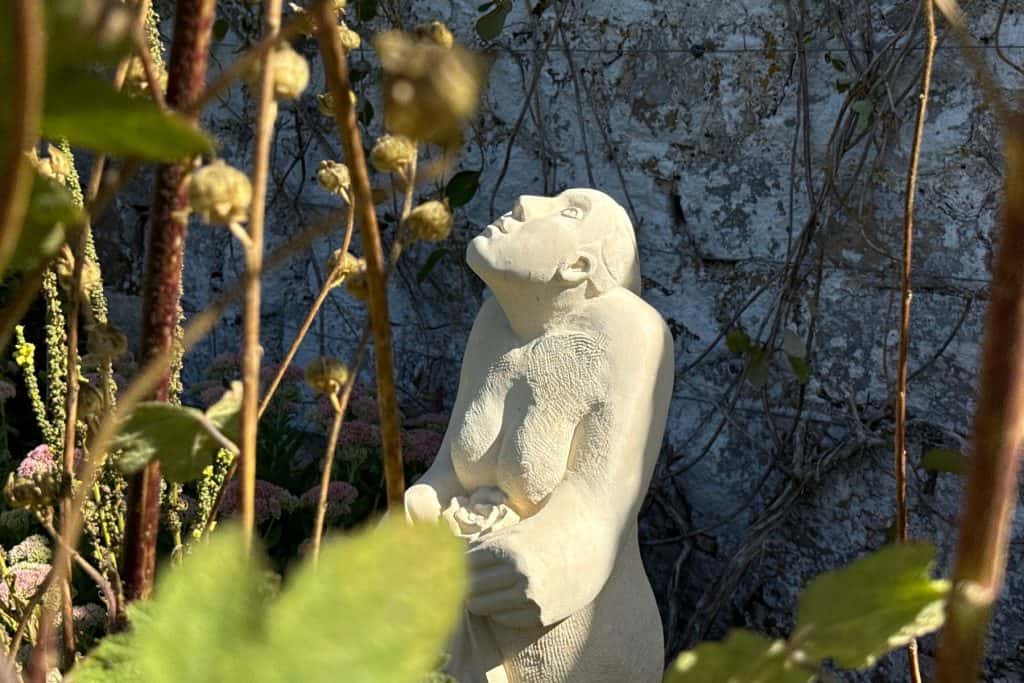 A stone sculpture of a woman holding a flower in the gardens of Avebury Manor