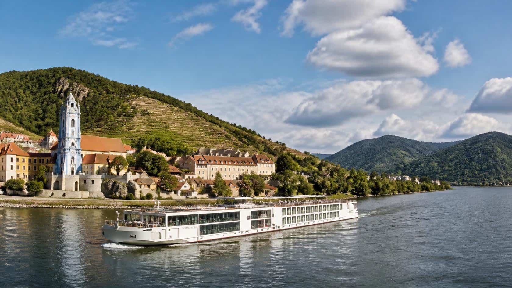 a river cruise ship sailing through Austria’s Wachau Valley. They feature the Danube, vineyard-covered hills, historic riverside villages, church towers, and a calm scenic atmosphere.
