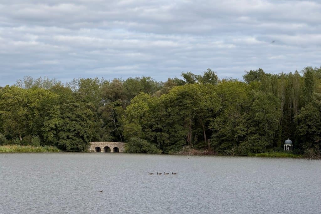 A view over the Big Lake towards a stone bridge in the grounds of Buscot Park in Oxforshire